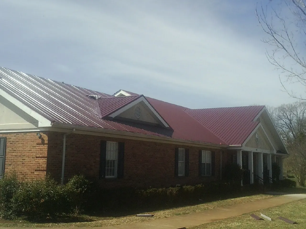 Red metal roof with gabled entries on a long brick building, from a Hail Damage Roof Repair job in Hermiston