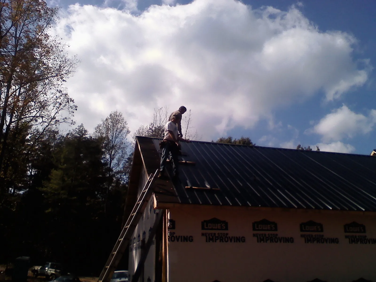 Roofer fastening dark metal panels high against a cloudy sky, from a Roof Inspection job in Hermiston