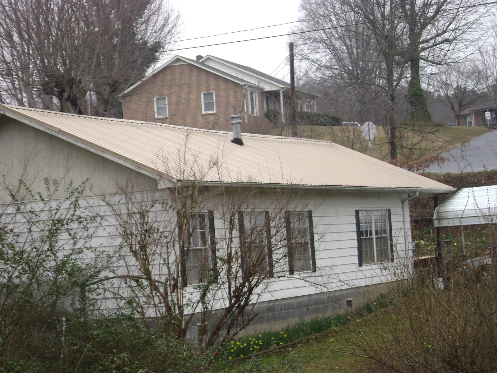 Tan metal roof on a white sided house set into a hillside — Commercial Roofing by Roofing Brothers in Hermiston